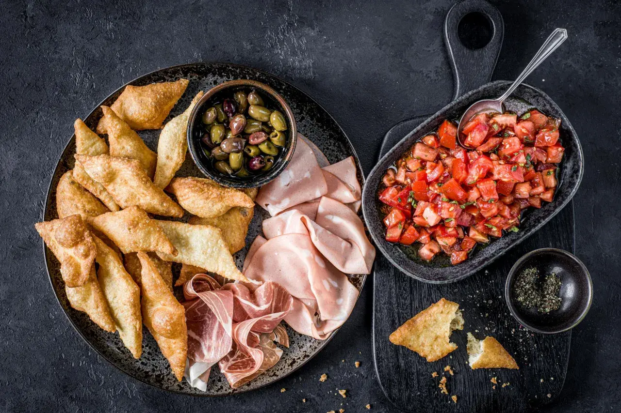 Assiette de gnocco fritto croustillant, olives, mortadelle et prosciutto, avec une salade de tomates fraîches.