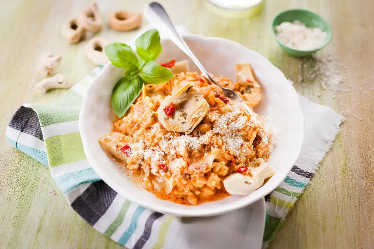 Un délicieux risotto pesto rosso, garni d'artichauts et de basilic frais, saupoudré de parmesan.