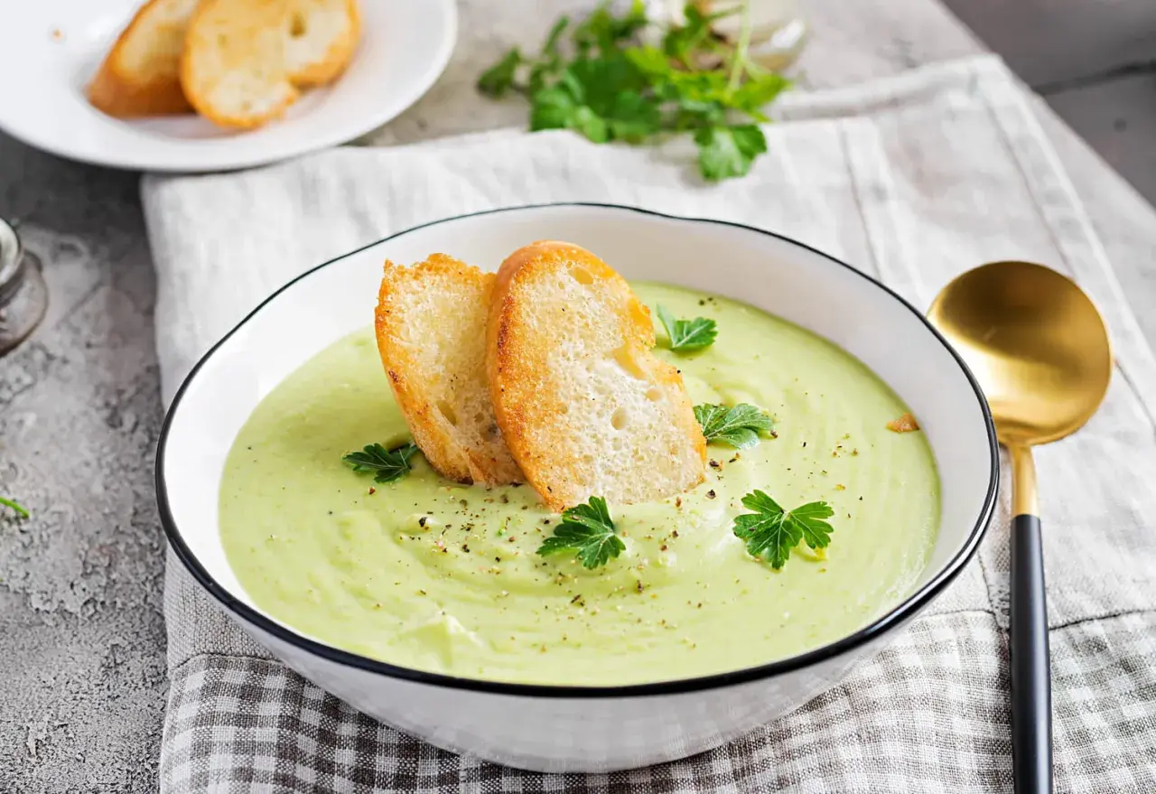 Un bol de soupe verte onctueuse, garnie de croûtons dorés et de persil frais. Parfait pour une recette gaspacho méditerranéen.