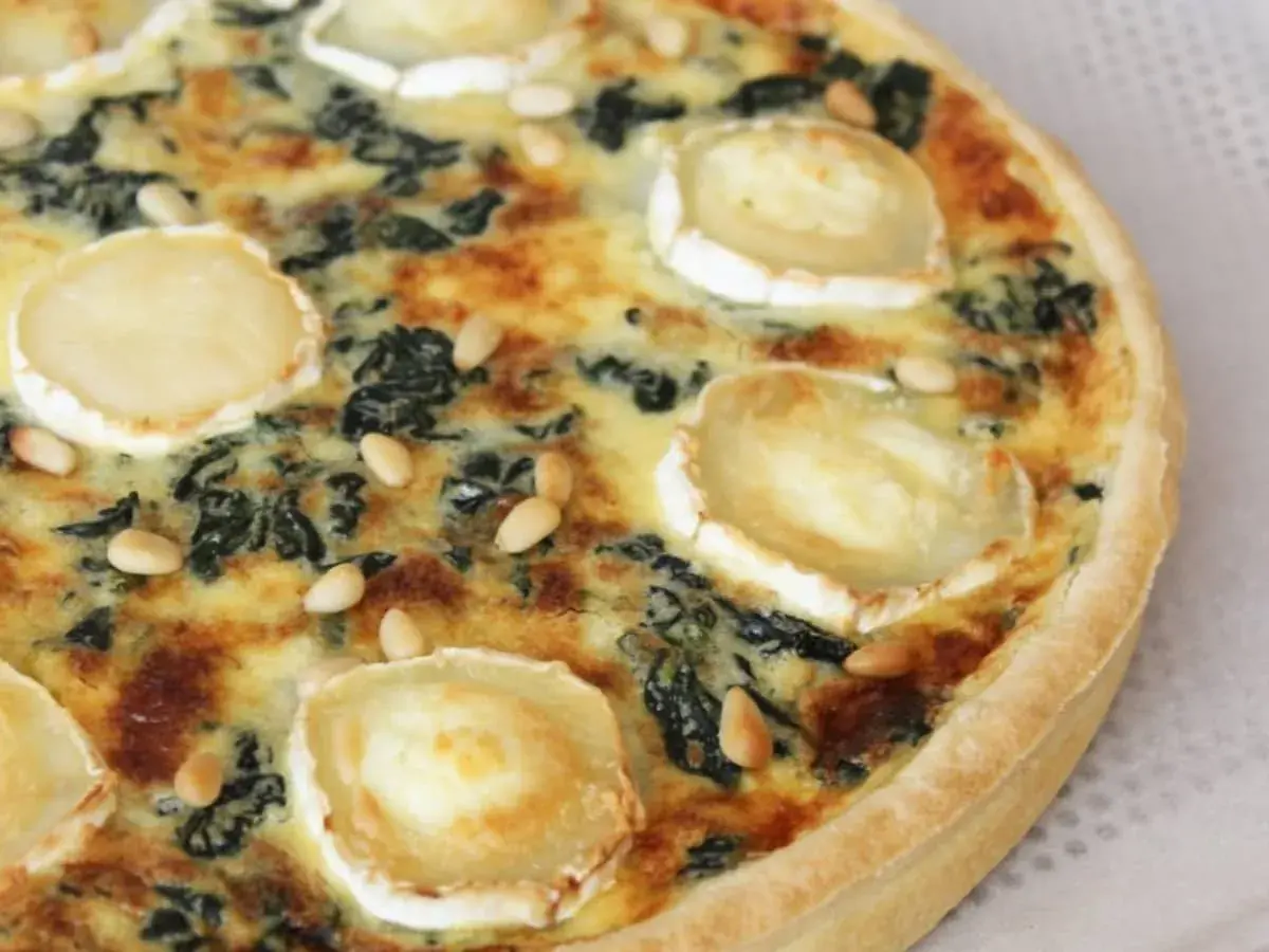 Quiche épinard chèvre, garnie de rondelles de fromage de chèvre et de pignons de pin, prête à être dégustée.