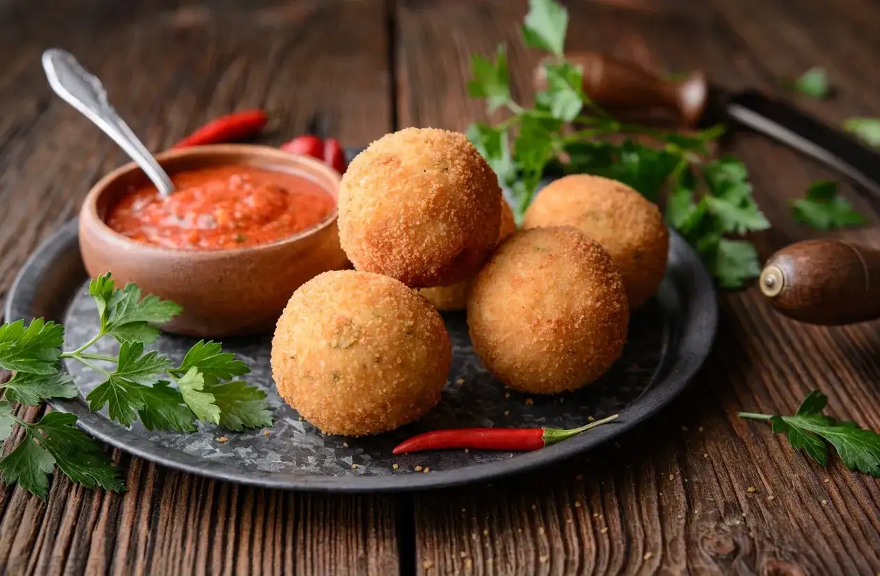Arancini dorés et croustillants, accompagnés de sauce tomate et de piment. Une recette parfaite pour un apéritif gourmand.