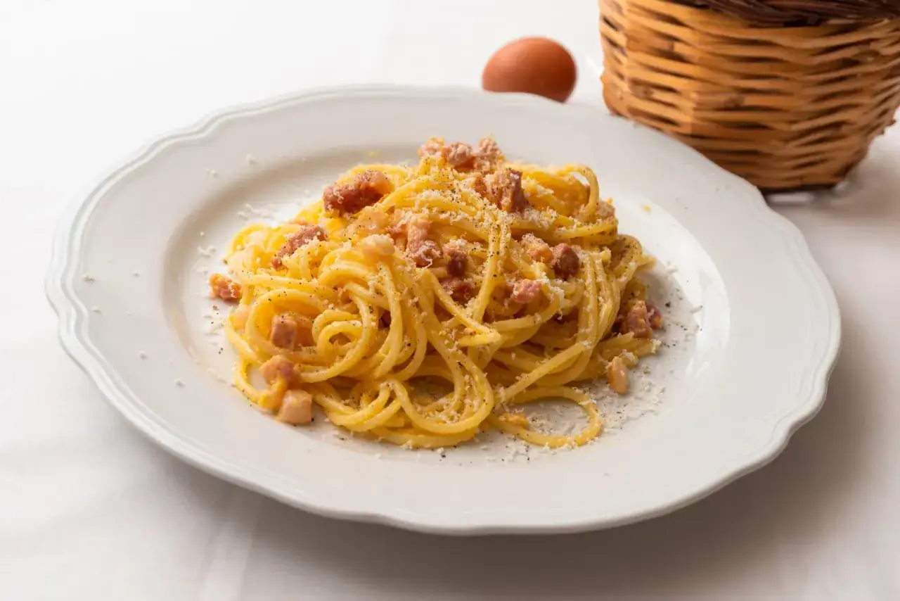 Une assiette de spaghetti crémeux, garnie de lardons et de parmesan, évoque la saveur authentique de la carbonara romaine.