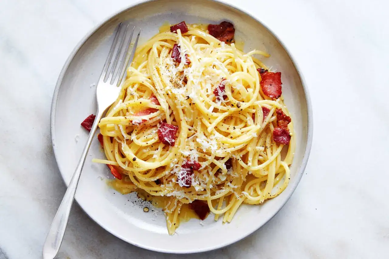 Une assiette de pâtes à la carbonara, garnie de lardons croustillants et de parmesan râpé, avec une fourchette prête à déguster.
