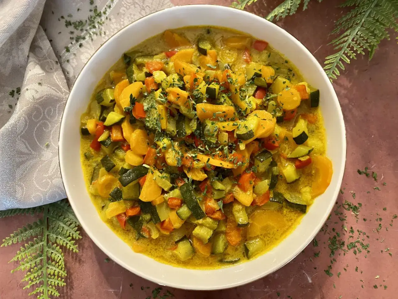 Un plat coloré de courgettes, carottes et poivrons dans une sauce crémeuse au curry, garni de persil frais.