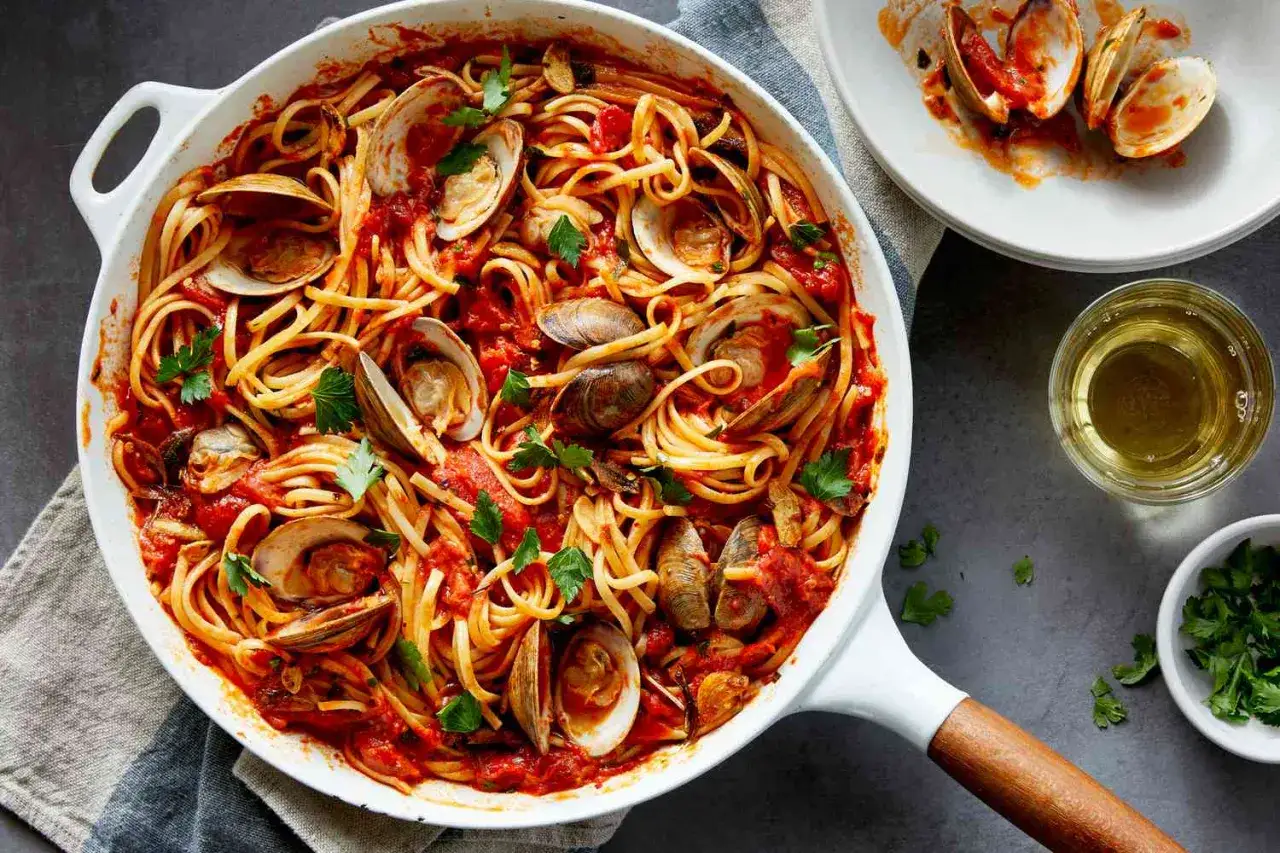 Un plat de spaghetti vongole tomate, garni de persil frais. Les palourdes s'ouvrent sur les pâtes dans une sauce rouge savoureuse.