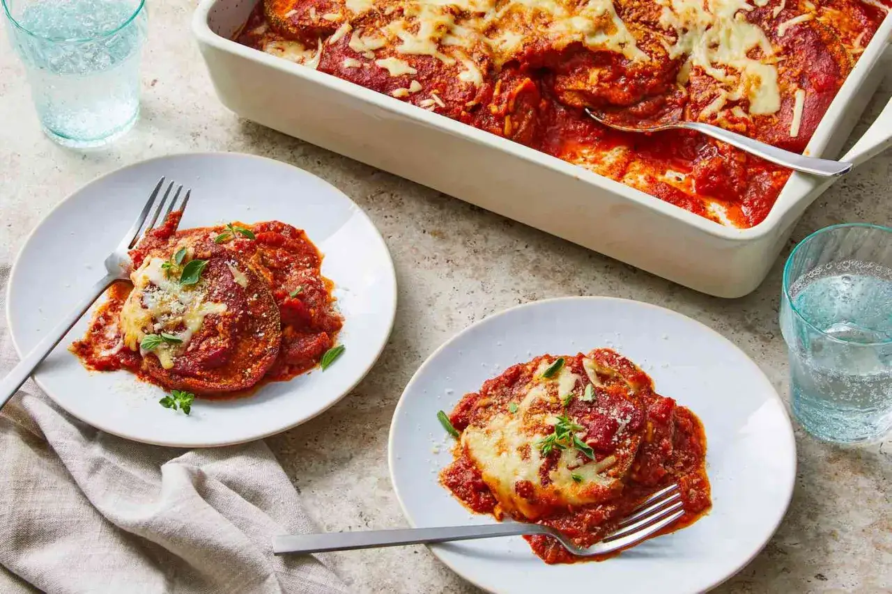 Deux assiettes de parmigiana d'aubergine, napp&eacute;es de sauce tomate et de fromage fondant, pr&ecirc;tes &agrave; &ecirc;tre d&eacute;gust&eacute;es.