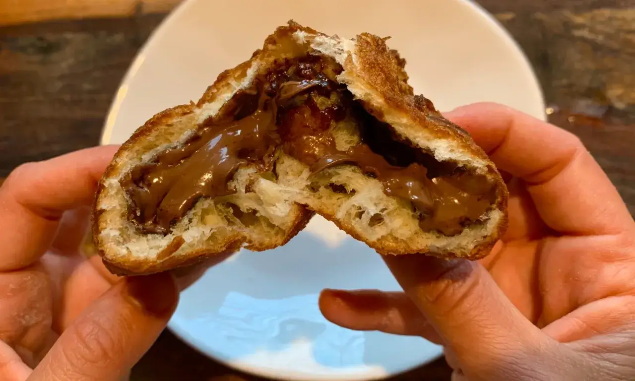 Deux mains tiennent un panzerotto ouvert, révélant une généreuse garniture de Nutella crémeux.
