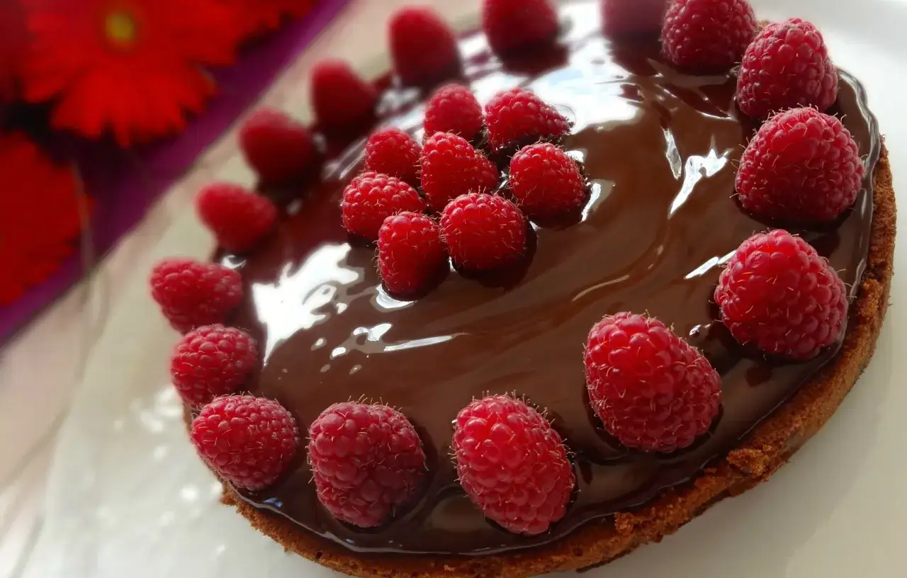 Gâteau gourmand fraise chocolat mascarpone, décoré de framboises fraîches sur un glaçage brillant.