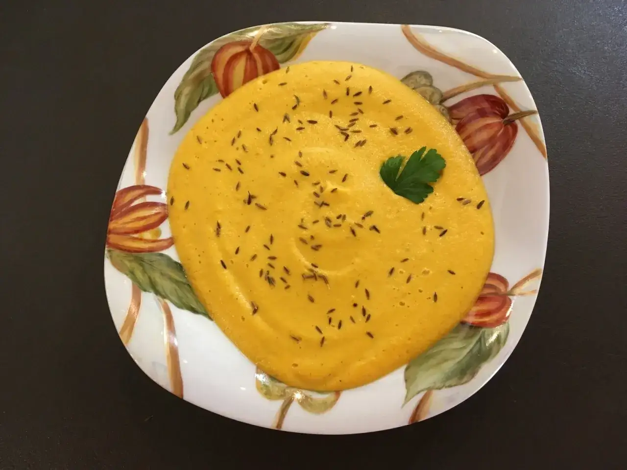 Purée de carotte on a decorative plate, sprinkled with cumin seeds and a parsley leaf.