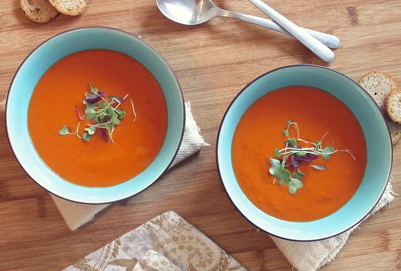 Deux bols de soupe froide &agrave; la tomate, garnie de jeunes pousses, sur une planche en bois avec des cro&ucirc;tons.