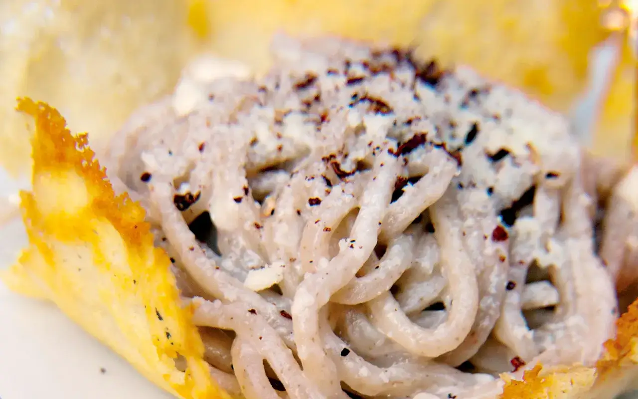 Un plat de tonnarelli cacio e pepe, des p&acirc;tes cr&eacute;meuses saupoudr&eacute;es de poivre noir, servies dans une coupe croustillante de fromage.