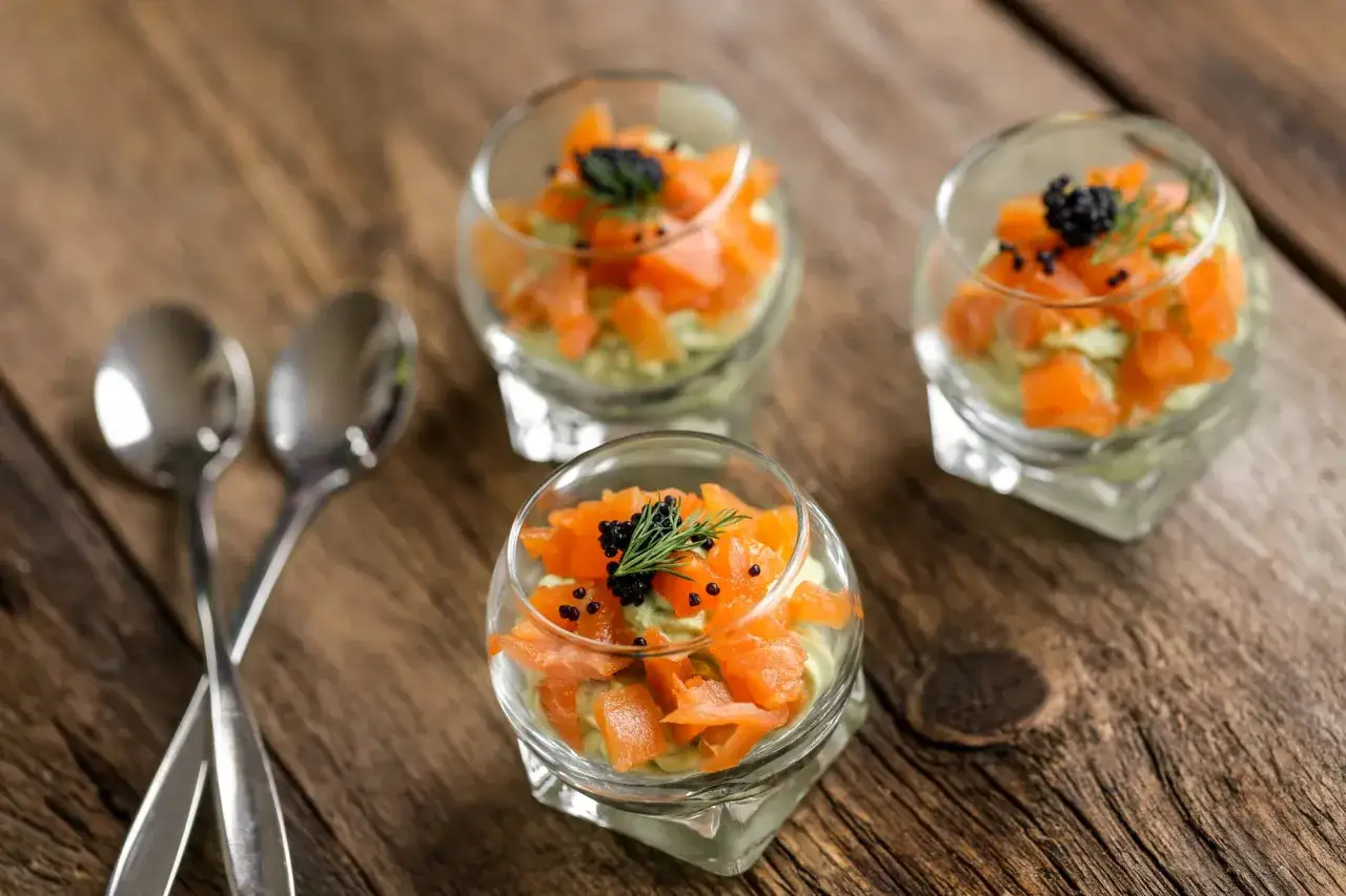 Trois verrines avocat saumon, garnies de caviar et d'aneth, sur une table en bois.