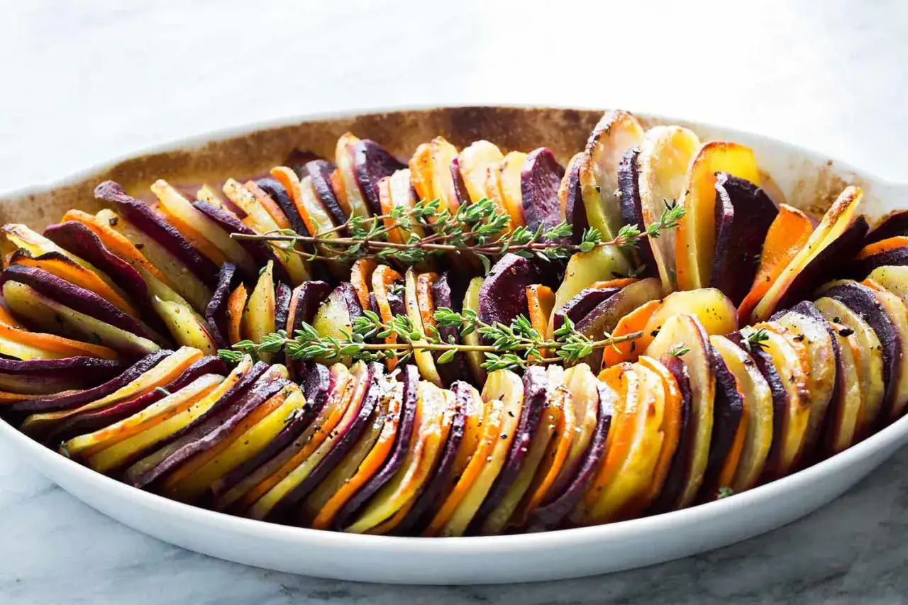 Gratin de légumes colorés, avec des rondelles de patate douce, carottes et betteraves, garni de thym frais.