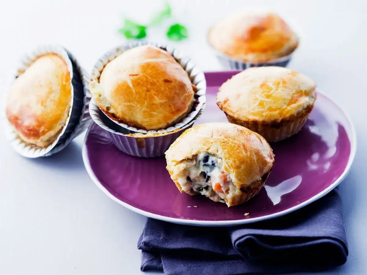 Quatre tourtes au poulet dor&eacute;es, une entam&eacute;e, sur une assiette violette.