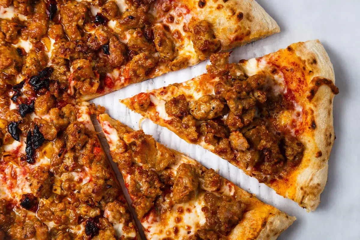 Une délicieuse pizza spianata piccante, garnie de morceaux de saucisse épicée et de fromage fondant, prête à être dégustée.