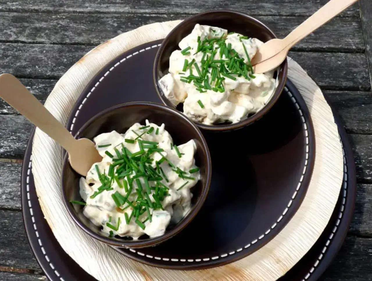 Deux bols de salade cr&eacute;meuse, parsem&eacute;e de ciboulette. Une cuill&egrave;re en bois repose dans chaque bol, pr&ecirc;ts &agrave; d&eacute;guster ces champignons &agrave; la cr&egrave;me.