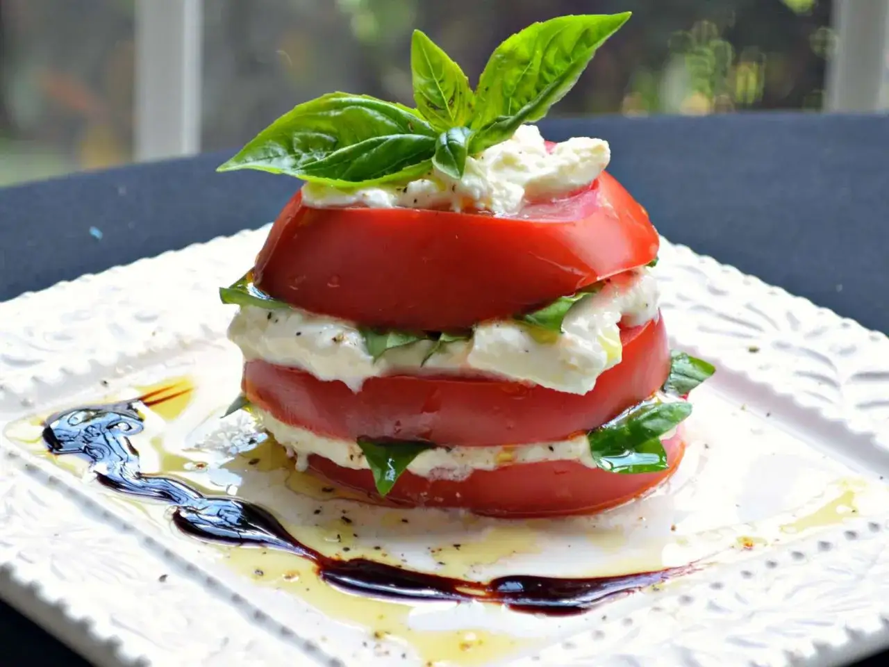 Délicieuse recette burrata froide : empilement de tomates rouges, mozzarella crémeuse et feuilles de basilic frais, arrosé d'huile d'olive et de vinaigre balsamique.