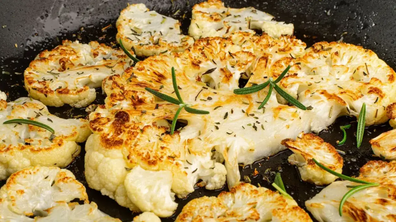 Tranches de chou-fleur dorées et herbacées dans une poêle, parfaites pour une recette facile et savoureuse.