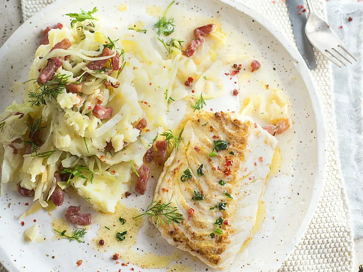 Filet de poisson blanc avec un écrasé de pomme de terre et des lardons, garni d'herbes fraîches et de poivre rose.