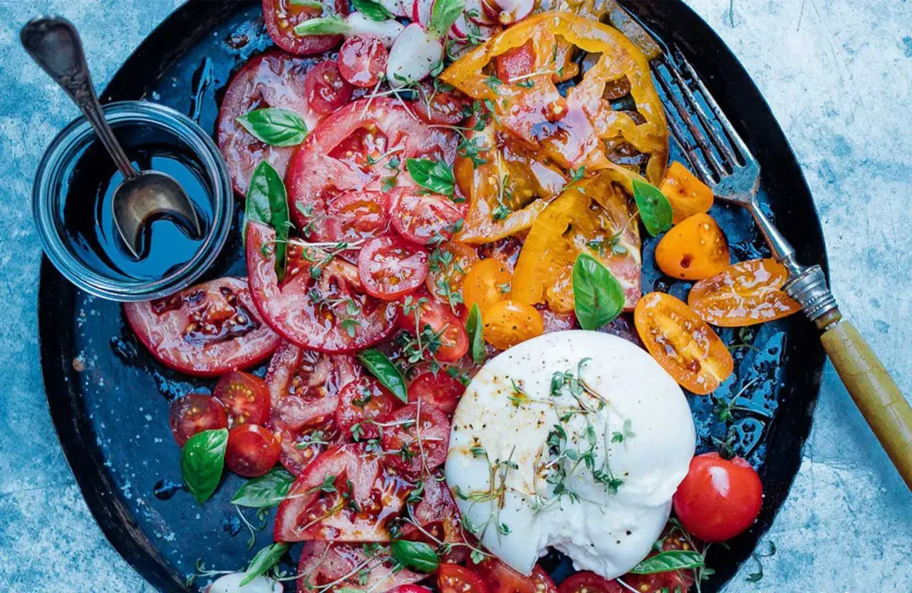 Salade estivale de tomates multicolores, burrata crémeuse et basilic frais, arrosée d'une vinaigrette acidulée, évoquant un caprese al limone.