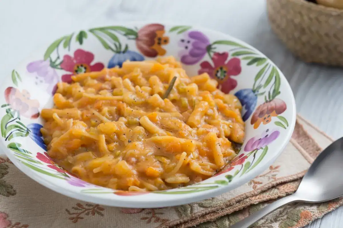 Un plat réconfortant de pasta e patate, un mélange de pâtes et de pommes de terre dans une sauce onctueuse, servi dans un bol décoré de fleurs.