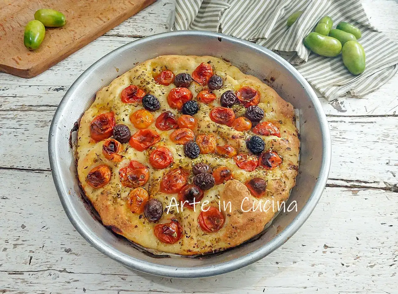 Focaccia barese dorée, garnie de tomates cerises et d'olives noires, prête à être dégustée.