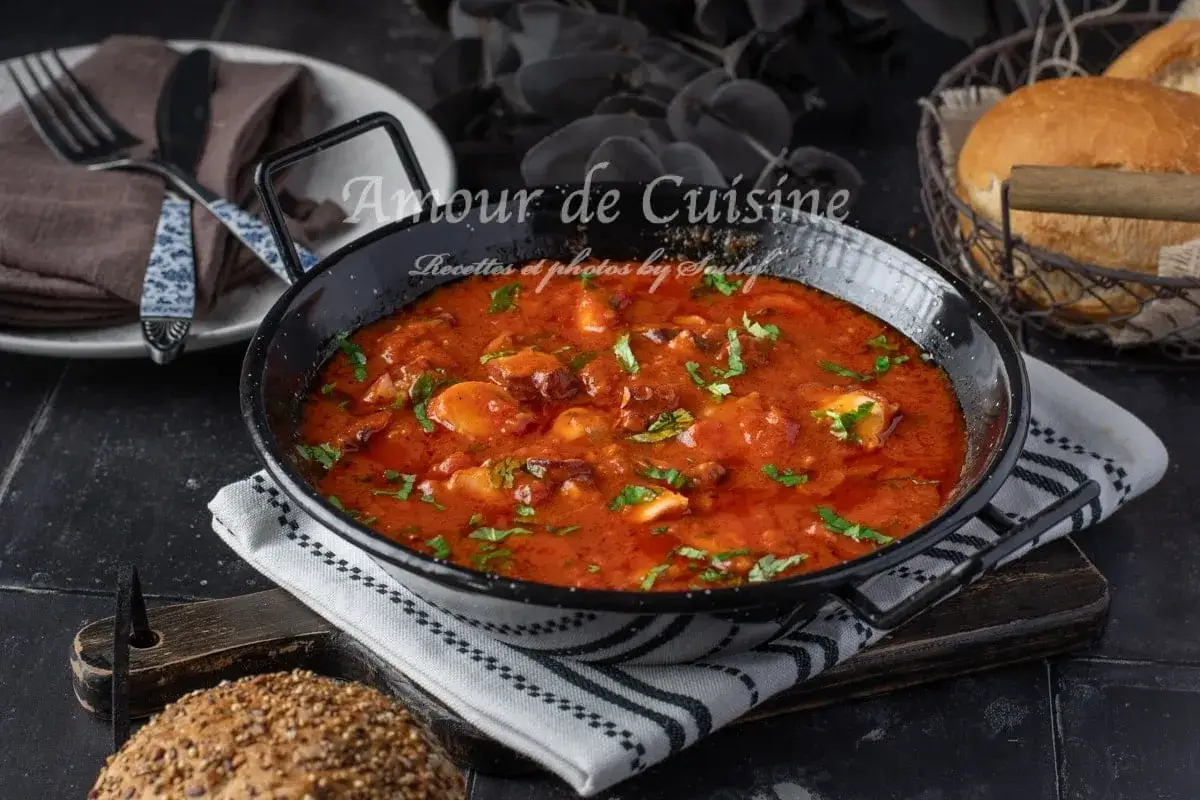 Un plat de p&acirc;tes au poulpe mijot&eacute; dans une sauce tomate savoureuse, garni de persil frais. Servi dans une po&ecirc;le noire, avec du pain en arri&egrave;re-plan.