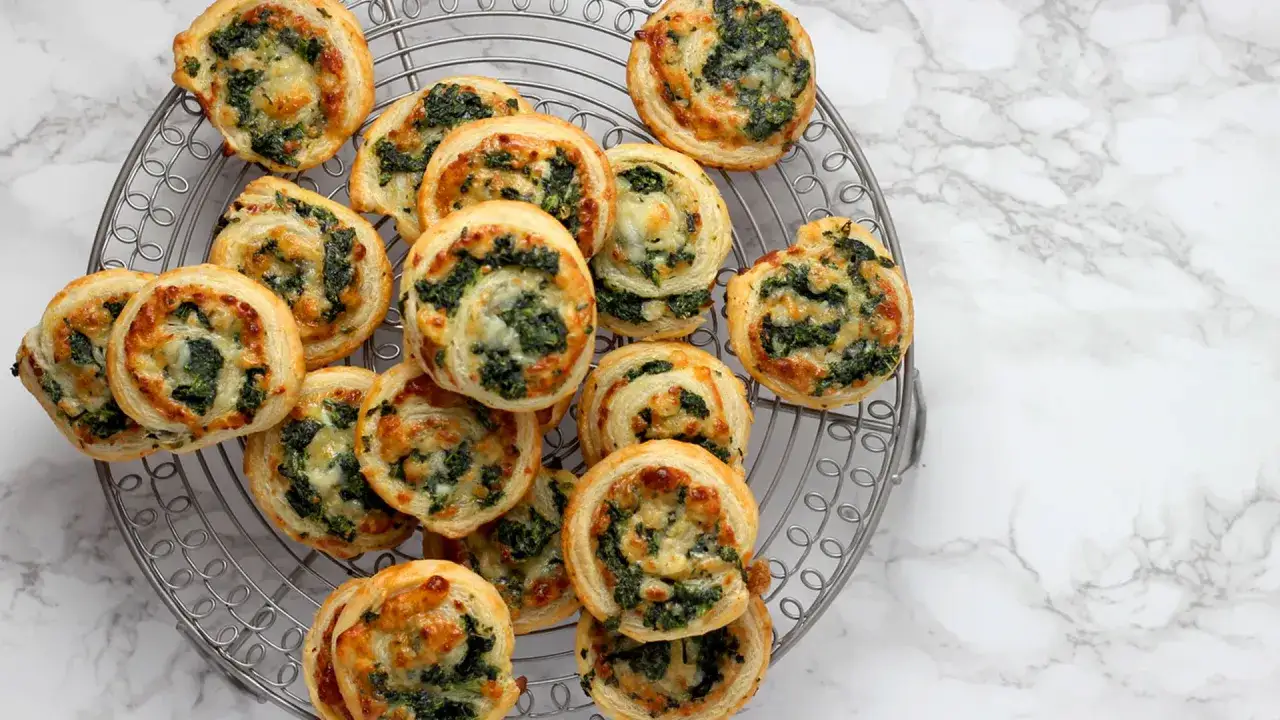 Petits roulés feuilletés à la tarte au fromage et aux épinards, dorés et appétissants, disposés sur une grille.