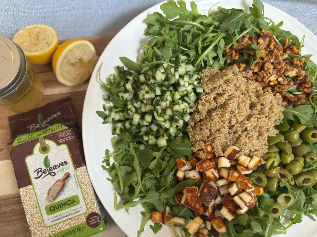 Salade color&eacute;e avec roquette, quinoa, concombre, olives, fromage grill&eacute; et noix. Une vinaigrette citronn&eacute;e et un paquet de quinoa sont &agrave; c&ocirc;t&eacute;.