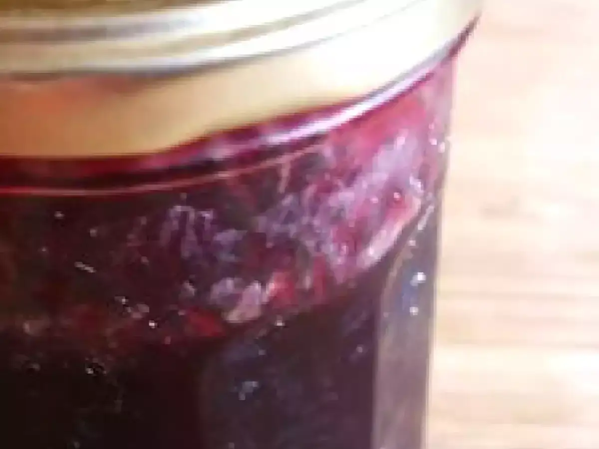 Un bocal de confiture de raisin noir, avec des morceaux de fruits visibles, prêt à être dégusté.