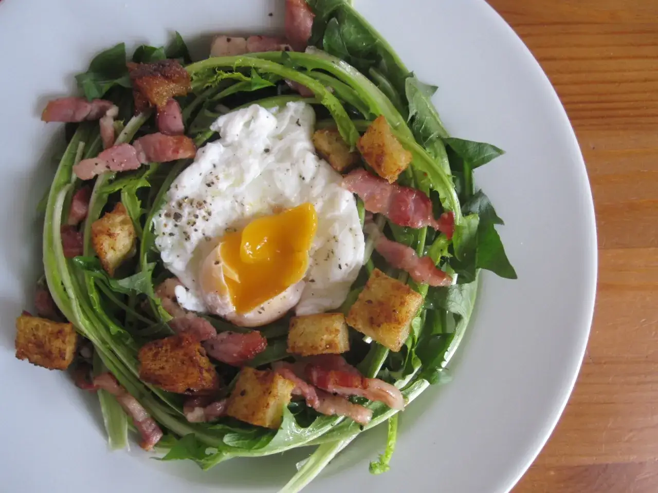 Salade lyonnaise avec œuf poché coulant, lardons croustillants et croûtons dorés sur un lit de verdure.