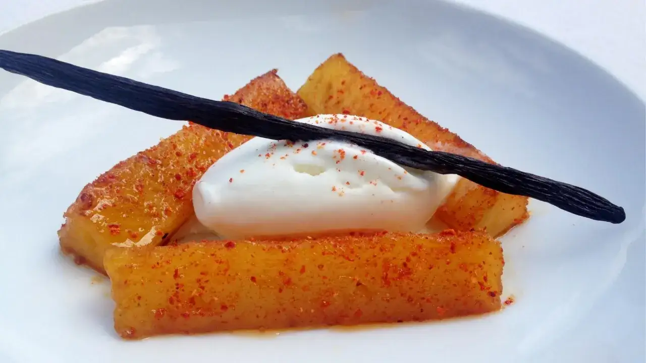 Délicieux dessert avec des morceaux de fruits caramélisés saupoudrés de confiture de piment, une boule de glace vanille et une gousse de vanille.