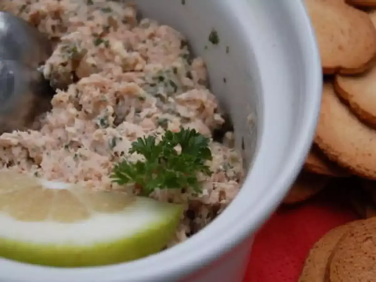 Un bol de rillettes de thon, garni d'une tranche de citron et de persil, prêt à être dégusté avec des toasts.
