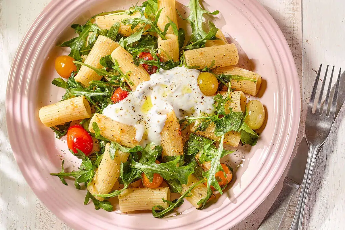 Pâtes rigatoni avec roquette, tomates cerises et une généreuse portion de burrata crémeuse, le tout assaisonné pour un plat de pâtes stracciatella parfait.
