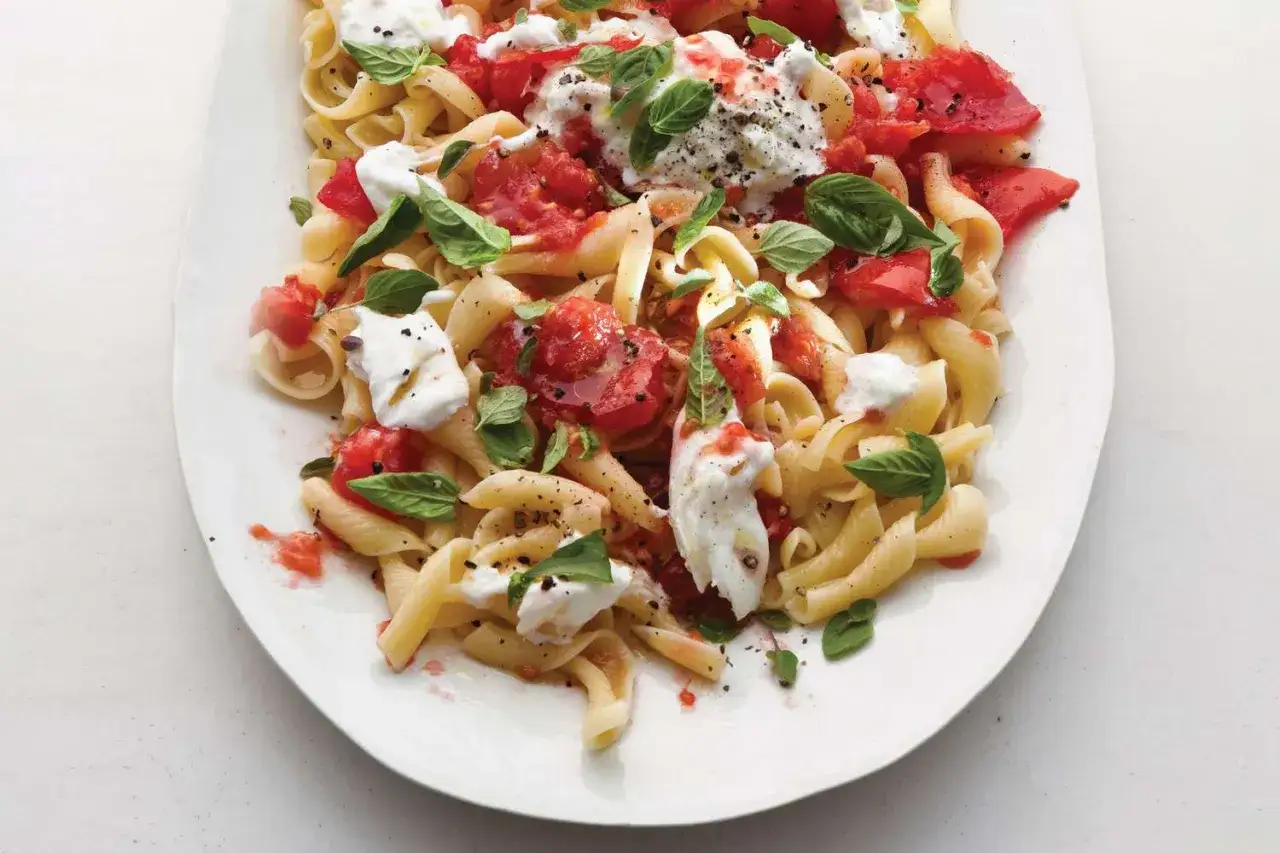 Un plat de pâtes alla checca, garni de tomates fraîches, de mozzarella fondante et de feuilles de basilic, prêt à être dégusté.