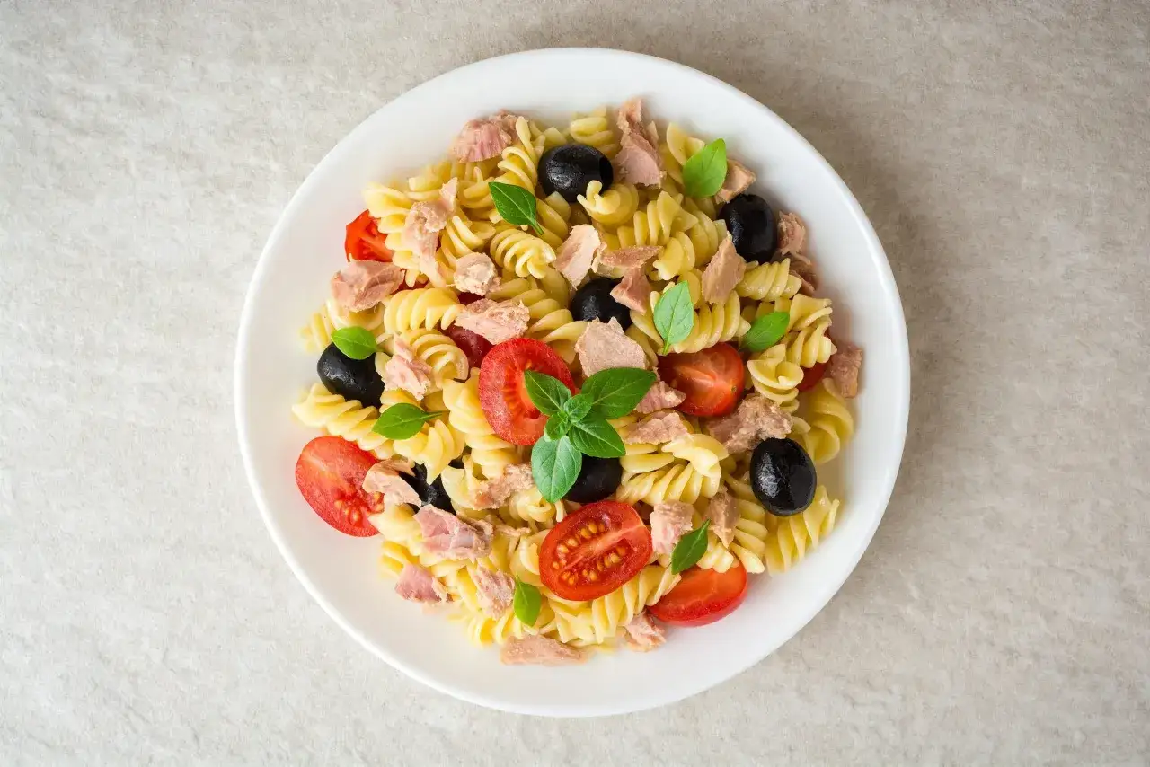 Salade de pâtes fusilli avec thon émietté, tomates cerises coupées, olives noires et feuilles de basilic frais. Une recette simple et savoureuse.