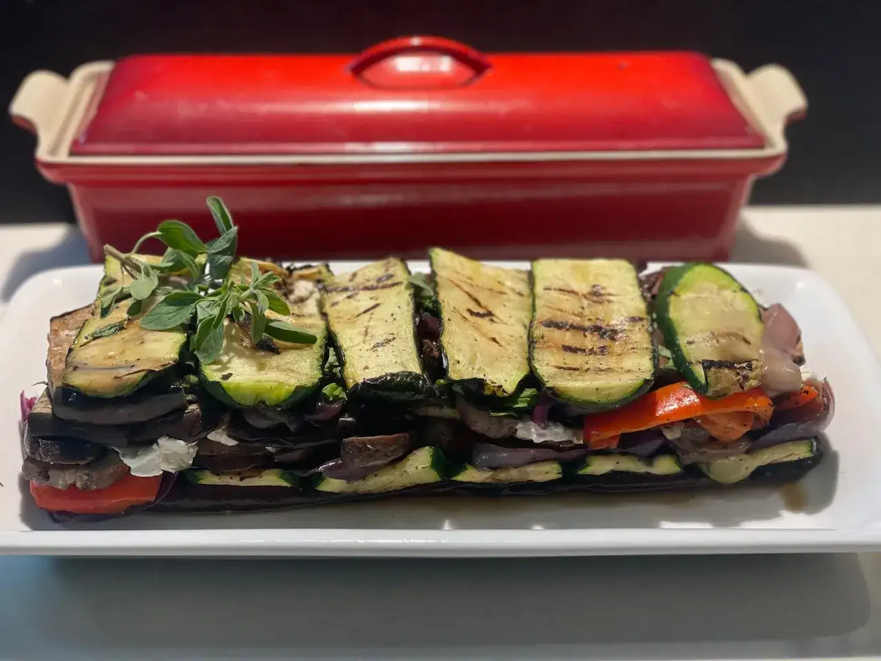 Délicieuse terrine de légumes grillés, empilant aubergines, courgettes et poivrons, garnie d'herbes fraîches. Un plat coloré et savoureux.