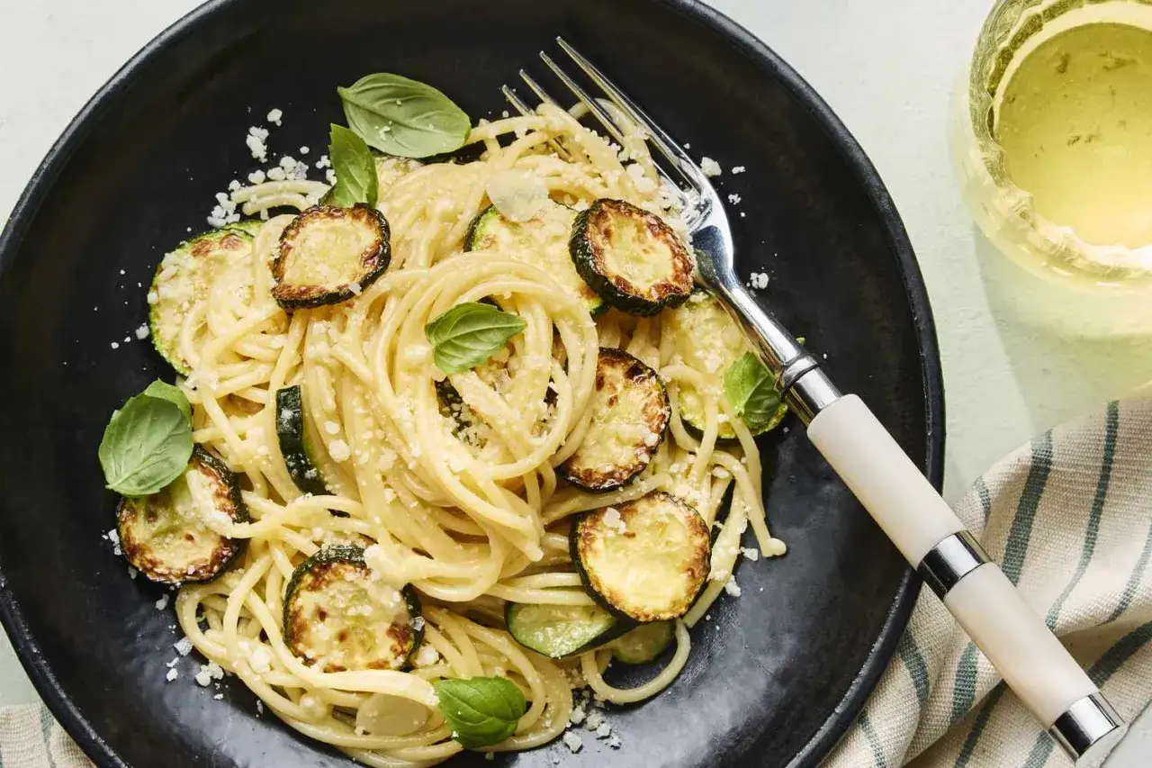 Spaghetti alla Nerano crémeux avec courgettes poêlées et basilic frais, servi dans une assiette noire.