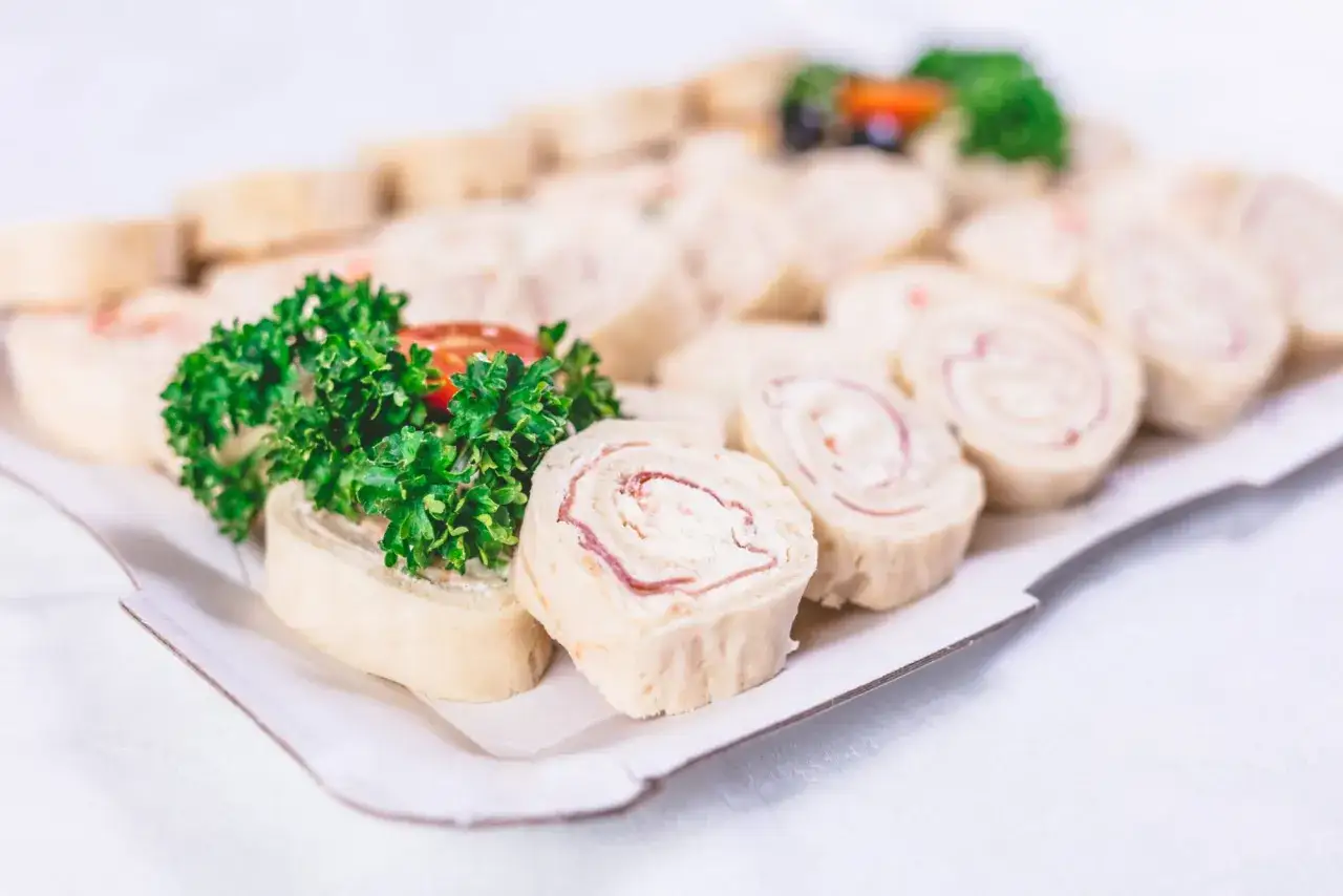 Plateau de wraps jambon, garni de persil frais et de tomates cerises. Ces petits rouleaux sont parfaits pour un apéritif.