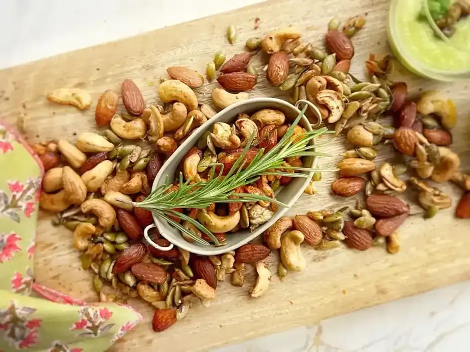 Un assortiment de noix et graines grillées, dont des amandes salées, garni de romarin frais.