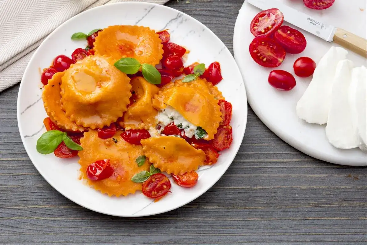 Raviolis Caprese orange vif, farcis de ricotta et basilic, servis avec des tomates cerises poêlées et une touche de mozzarella fraîche.