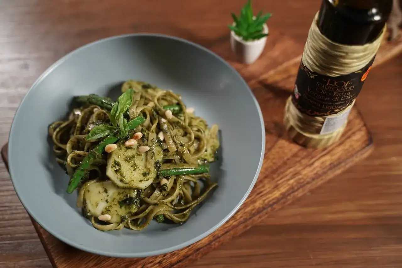 Assiette de trenette al pesto, garnie de haricots verts, pignons de pin et basilic. Une bouteille d'huile d'olive est visible &agrave; c&ocirc;t&eacute;.