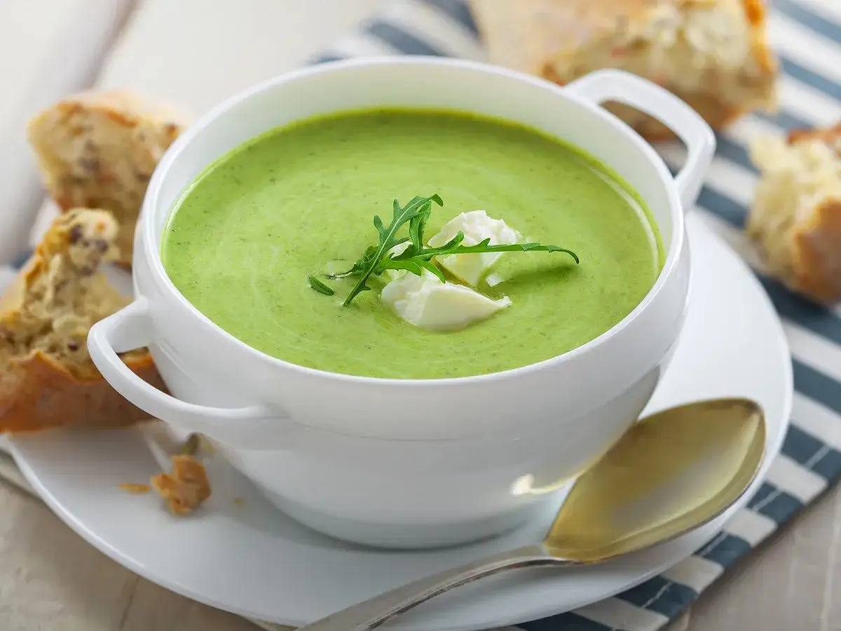 Soupe froide courgette fromage frais, garnie de roquette, servie avec du pain croustillant.