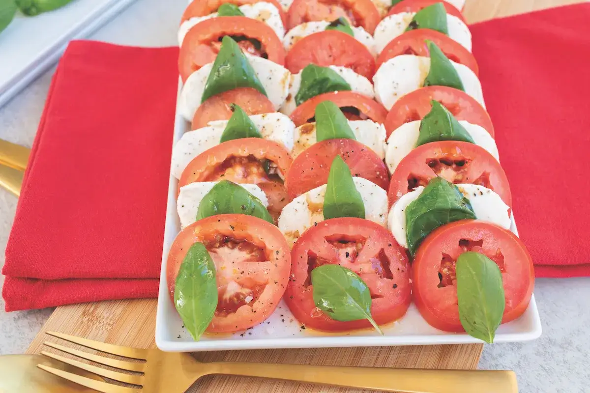 Une belle salade italienne, composée de tranches de tomates rouges, de mozzarella blanche et de feuilles de basilic vert frais, arrosée d'une vinaigrette.