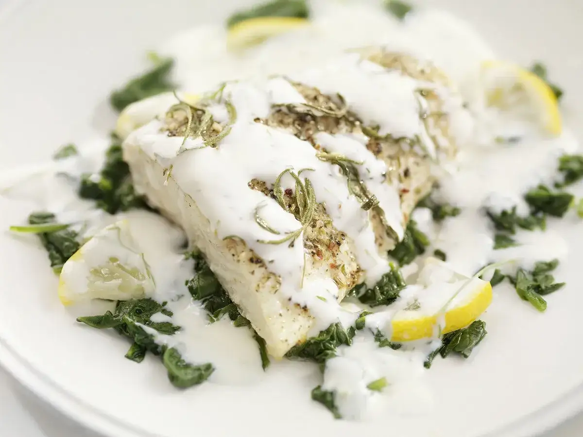 Un filet de poisson napp&eacute; d'une sauce cr&eacute;meuse, servi sur un lit d'&eacute;pinards &agrave; la cr&egrave;me, garni de romarin et de quartiers de citron.