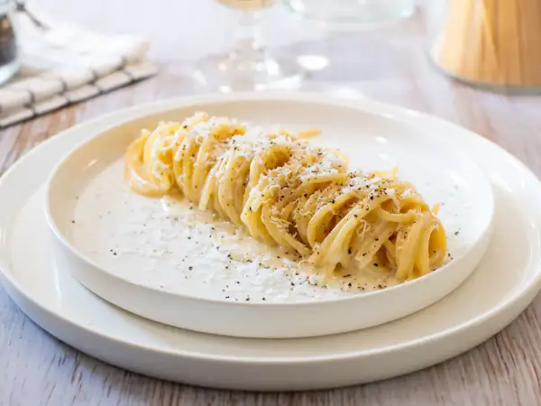 Un plat de tonnarelli cacio e pepe, des pâtes crémeuses saupoudrées de fromage et de poivre noir, sur une assiette blanche.