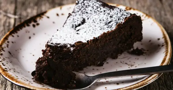 Une part de torta tenerina, un gâteau au chocolat intense, saupoudrée de sucre glace, sur une assiette rustique.
