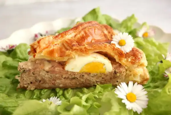 Tranche de pâté de Pâques savoureux, garni d'un œuf dur, sur un lit de salade verte et décoré de pâquerettes.