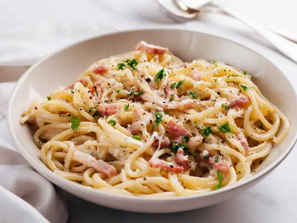 Un plat de carbonara romaine crémeuse, garni de lardons, de persil frais et de parmesan râpé. Un délice !