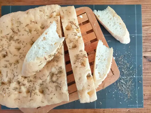 Délicieuse focaccia sans gluten, parsemée de romarin et de sel, coupée en tranches sur une planche en bois.